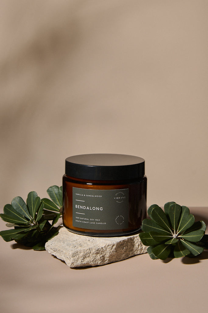Brown Bendalong candle jar with black lid on a stone surface with green leaves, against a beige background