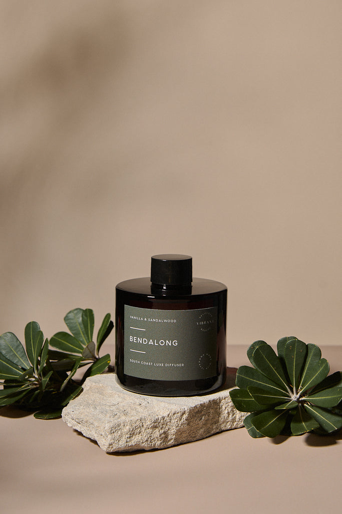 Amber glass reed diffuser labelled 'Bendalong' on a stone surface with green leaves on a beige background