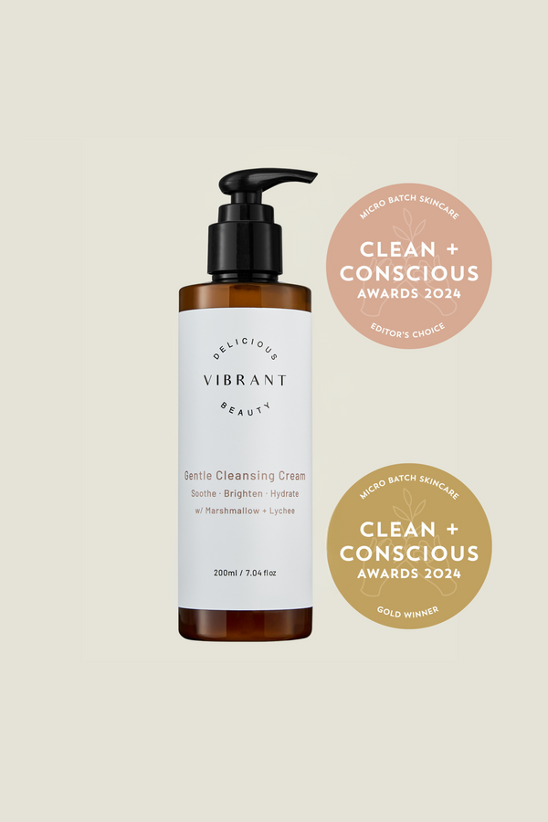 Bottle of 'Delicious Vibrant Beauty' cleansing cream with awards on a beige background