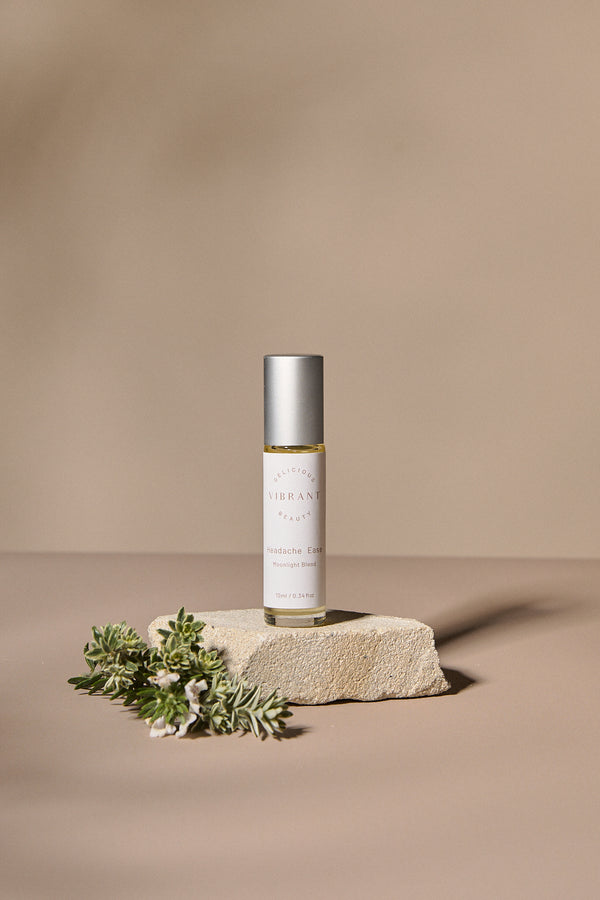 Headache Ease roller bottle with greenery on a beige background