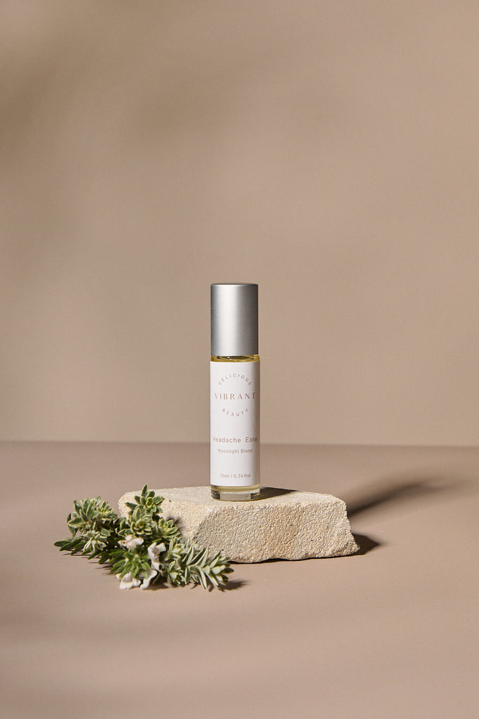 Headache Ease roller bottle with greenery on a beige background