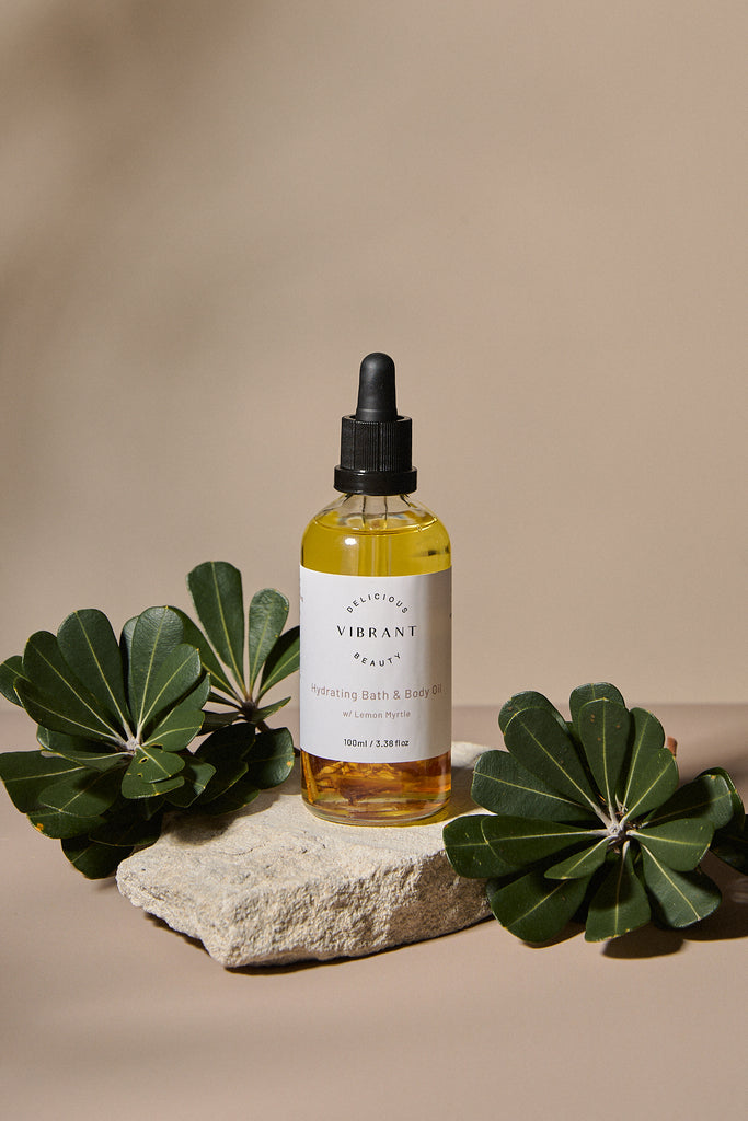 Bottle of Hydrating Bath & Body oil on a stone surface with green leaves.