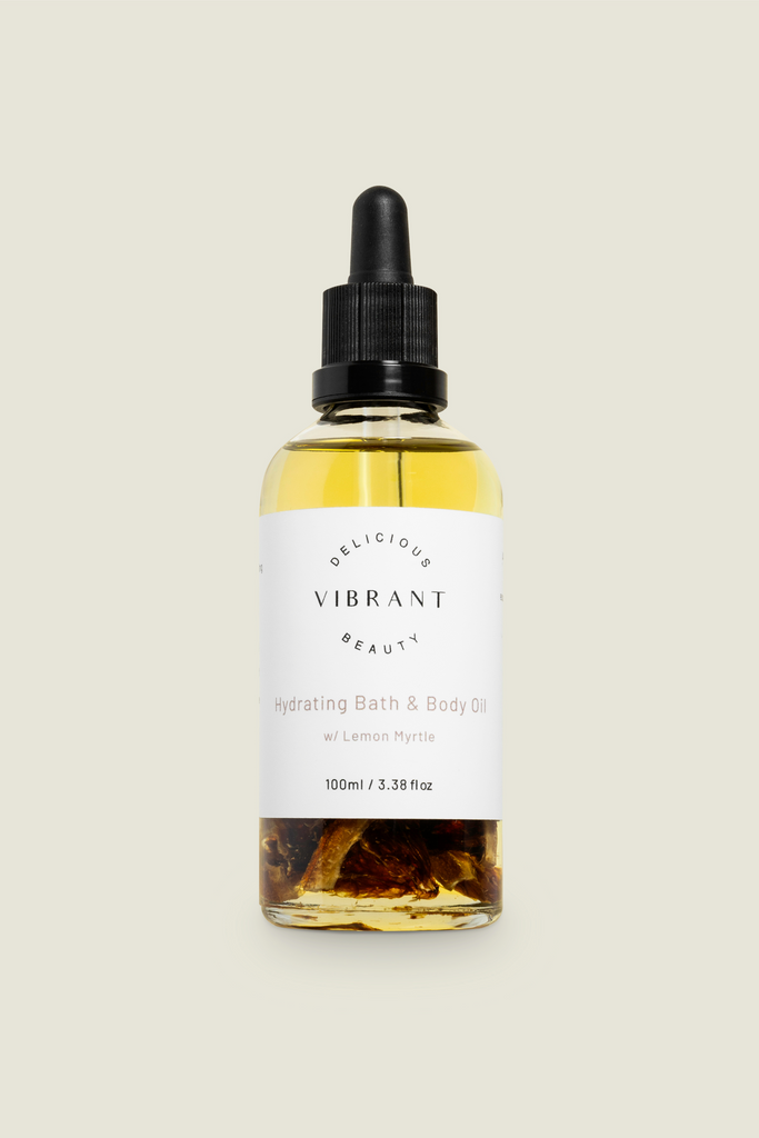 A clear glass bottle with a dropper, labelled 'DELICIOUS VIBRANT BEAUTY Hydrating Bath & Body Oil', with visible golden oil inside.