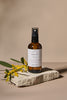 Brown spray bottle labelled Hydrating Toning Mist on a stone surface with yellow flowers on a beige background