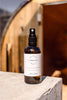 Bottle of 'Delicious Vibrant Beauty' toning mist on a concrete ledge with blurred sauna background