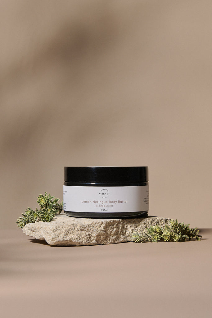 Jar of lemon meringue body butter on a stone surface with a blurred background