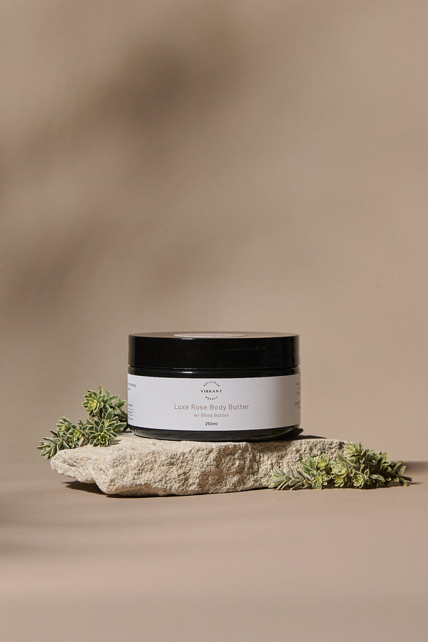 Jar of Luxe Rose body butter on a stone surface with a natural background