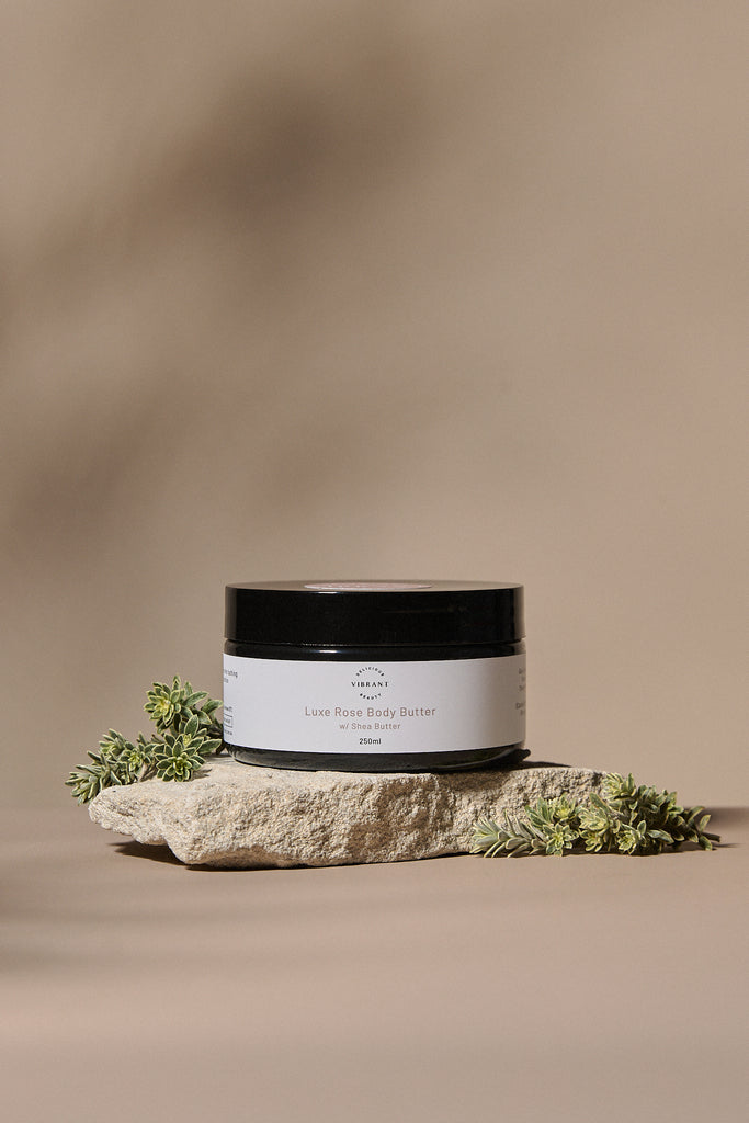 Jar of Luxe Rose body butter on a stone surface with a natural background