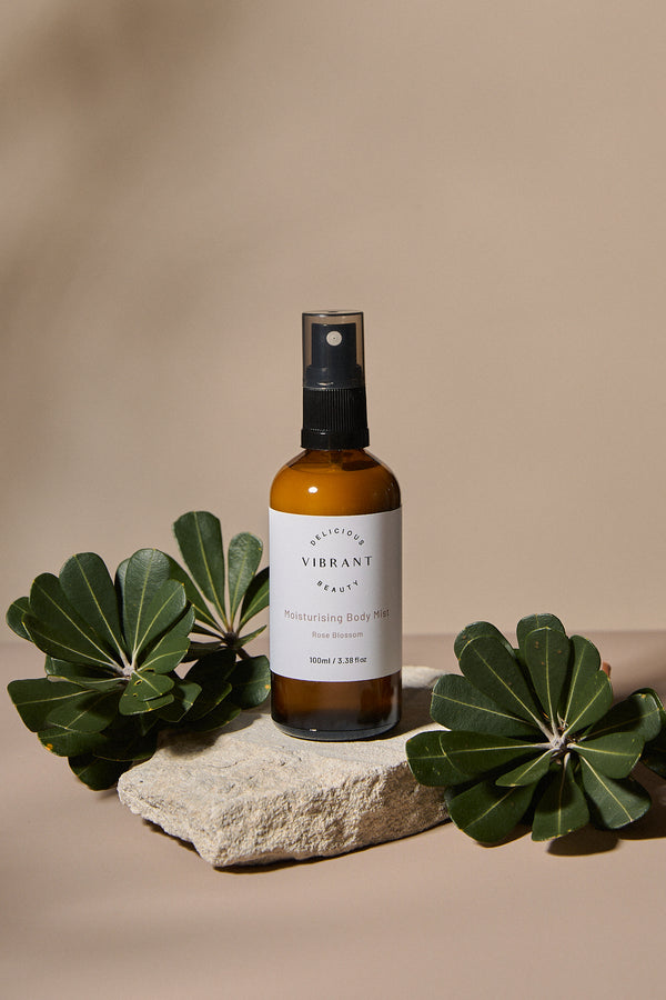 Bottle of 'Delicious Vibrant Beauty' product on a stone surface with green leaves on a beige background