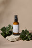 Bottle of 'Delicious Vibrant Beauty' product on a stone surface with green leaves on a beige background