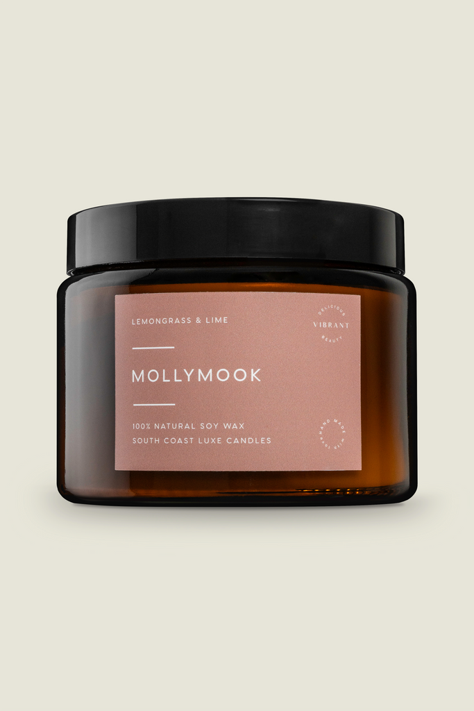 A Mollymook branded candle with lemongrass and lime scent, packaged in a clear jar with a black lid and a label, indicating it is a 100% natural soy wax candle with a double wick and an 80-hour burn time.
