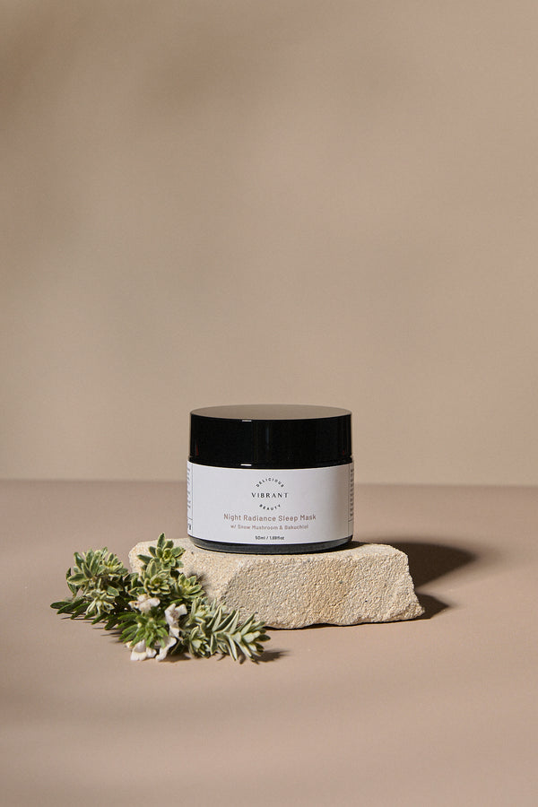 Jar Night Radiance Sleep Mask with a black lid on a beige stone block against a beige background