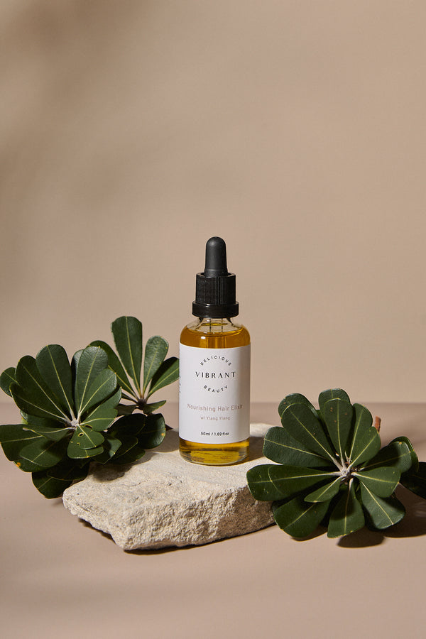 Bottle of Nourishing Hair Elixir oil with green leaves on a beige background