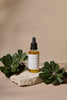 Bottle of Nourishing Hair Elixir oil with green leaves on a beige background