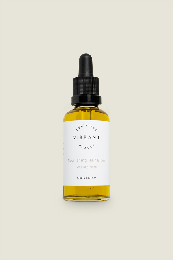 A clear glass bottle with a dropper, labelled 'DELICIOUS VIBRANT BEAUTY Hair Elixir', filled with yellow liquid.