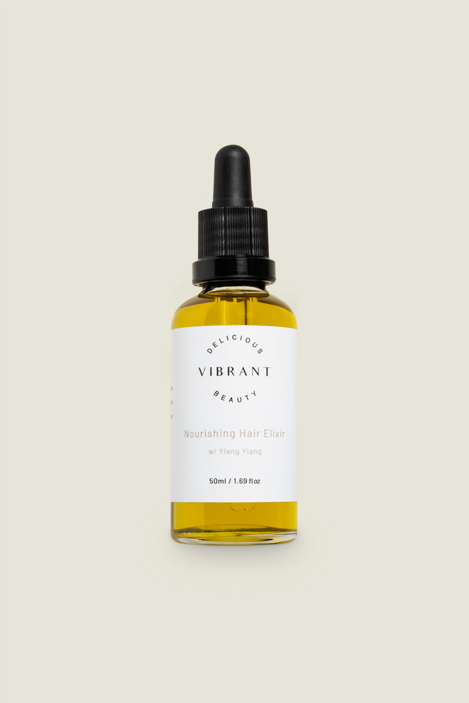 A clear glass bottle with a dropper, labelled 'DELICIOUS VIBRANT BEAUTY Hair Elixir', filled with yellow liquid.