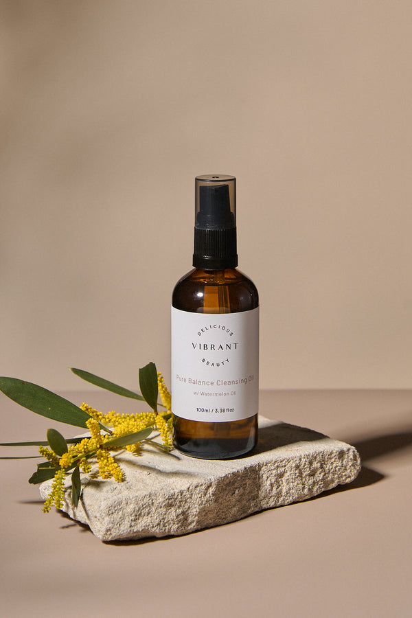 Bottle of 'Pure Balance Cleansing Oil skincare product on a stone surface with wattle lowers & leaves.