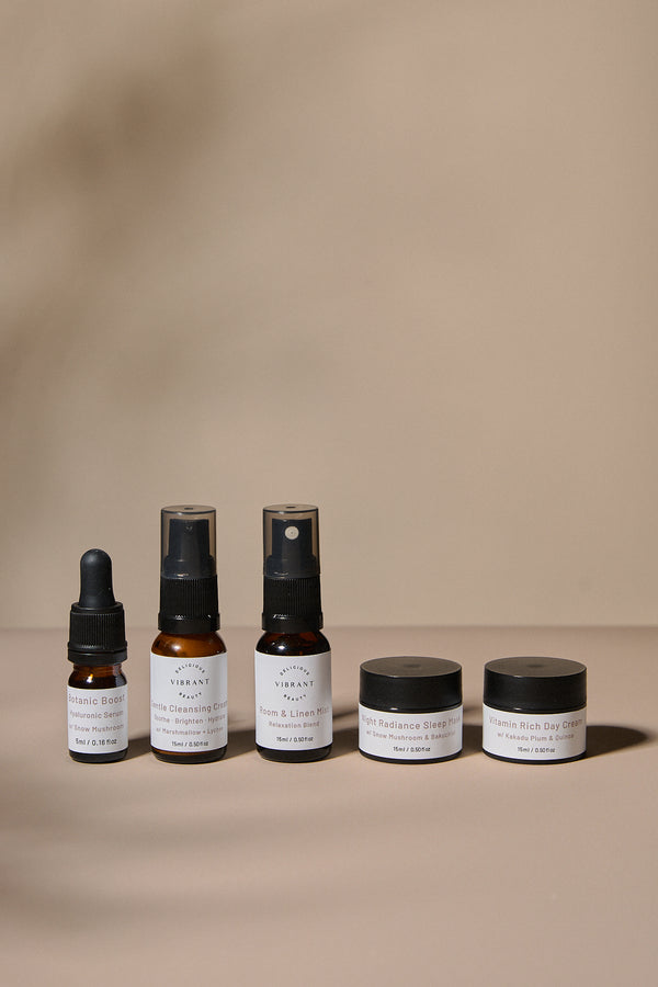 Set of Delicious Vibrant Beauty mini sized skincare products including bottles and jars on a beige background