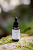 Bottle of Rosacea Rescue Solution skincare product on a mossy rock with a blurred natural background
