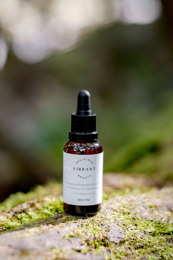 Bottle of Rosacea Rescue Solution skincare product on a mossy rock with a blurred natural background