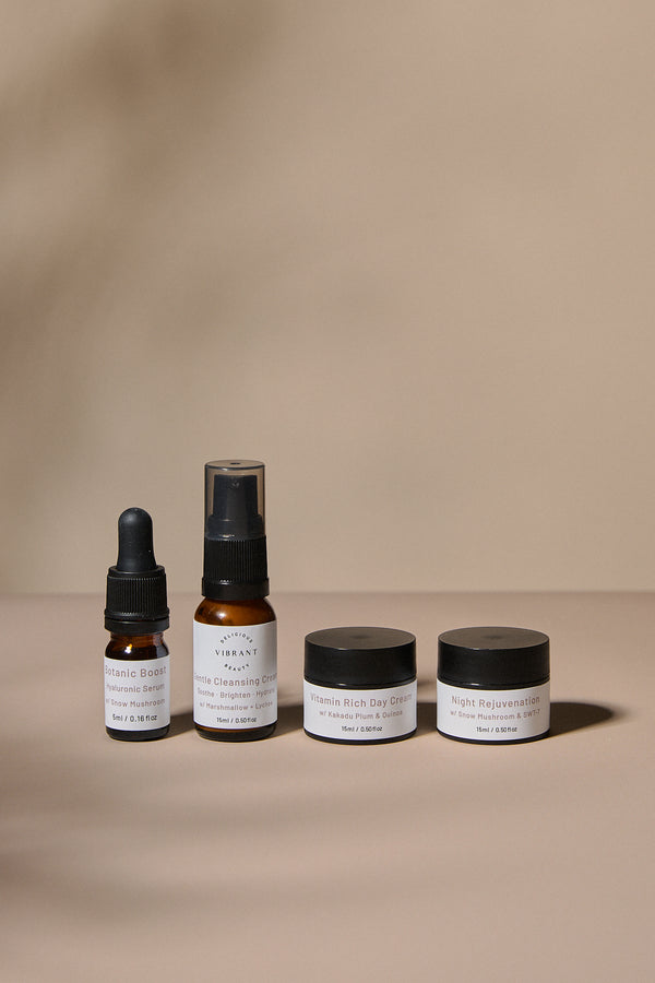 Set of Delicious Vibrant Beauty mini sized skincare products including bottles and jars on a beige background